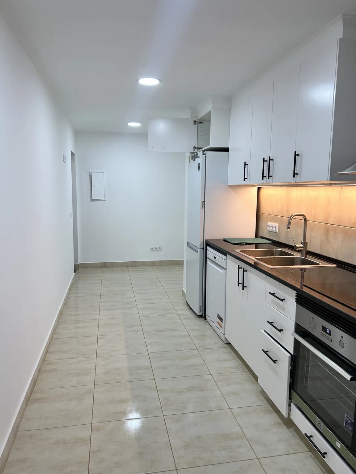Cozinha remodelada com móveis brancos e iluminação embutida